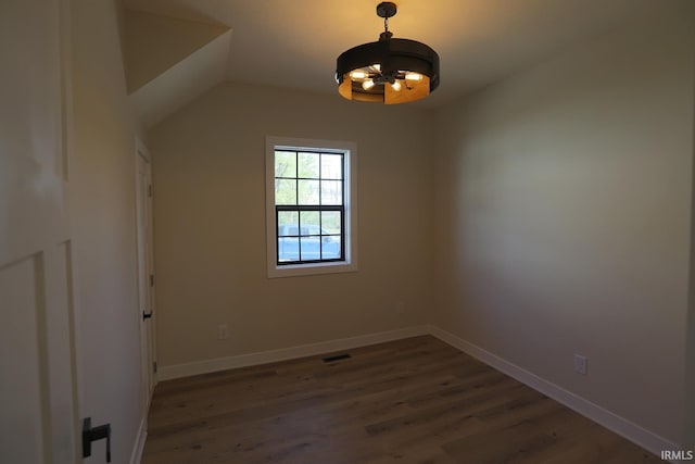 empty room featuring a chandelier, wood finished floors, baseboards, and vaulted ceiling