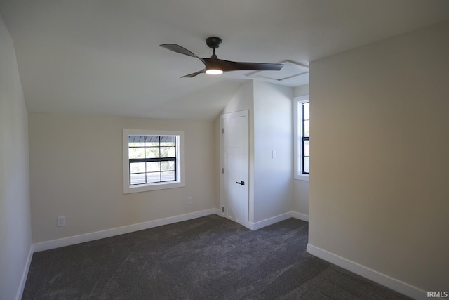 unfurnished room with dark colored carpet, vaulted ceiling, a ceiling fan, and baseboards