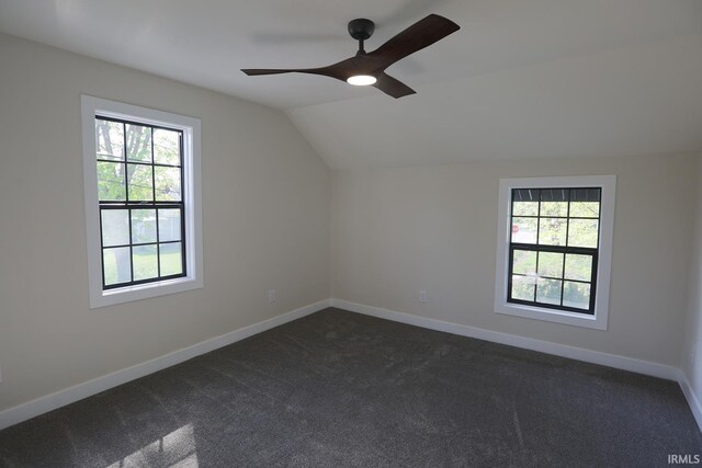 bonus room with plenty of natural light, vaulted ceiling, a ceiling fan, dark colored carpet, and baseboards