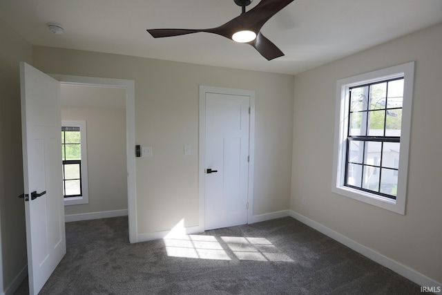 unfurnished bedroom with multiple windows, dark colored carpet, and baseboards