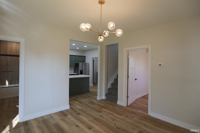 unfurnished dining area featuring a chandelier, wood finished floors, stairway, and baseboards
