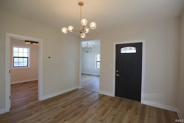 foyer featuring a chandelier, healthy amount of natural light, wood finished floors, and baseboards