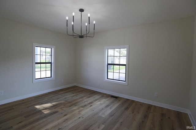 empty room featuring a chandelier, wood finished floors, and baseboards