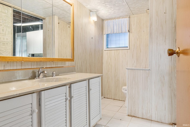 bathroom featuring toilet, vanity, tile patterned floors, and wood walls