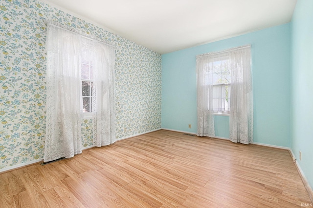 empty room featuring wallpapered walls, wood finished floors, and baseboards