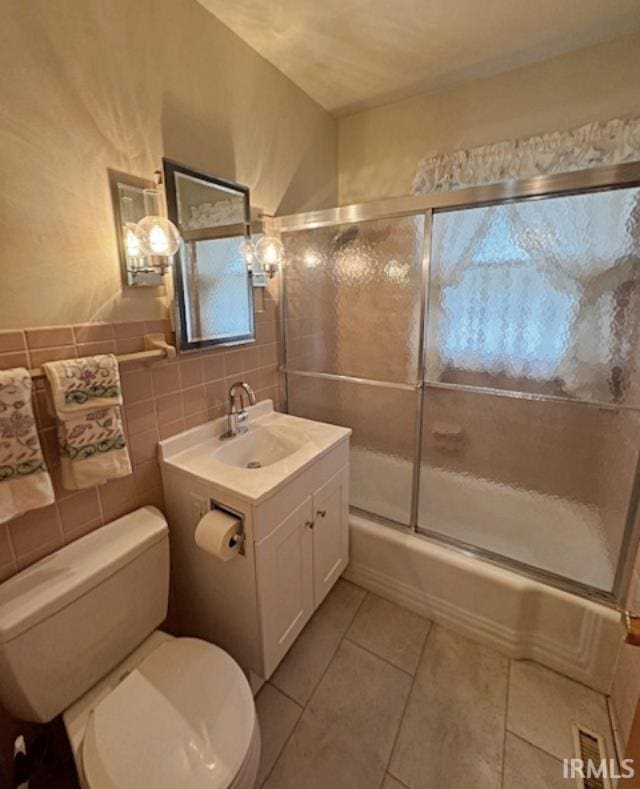 full bathroom featuring toilet, tile patterned floors, bath / shower combo with glass door, vanity, and tile walls