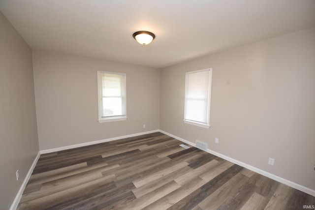 unfurnished room featuring plenty of natural light, dark wood-type flooring, and baseboards