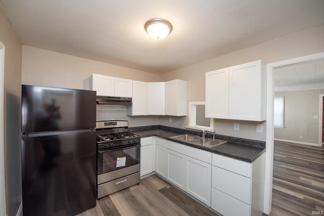 kitchen featuring freestanding refrigerator, stainless steel range with gas stovetop, under cabinet range hood, a sink, and dark countertops
