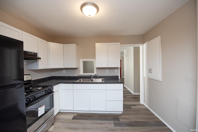 kitchen with freestanding refrigerator, range with gas stovetop, a sink, under cabinet range hood, and white cabinets