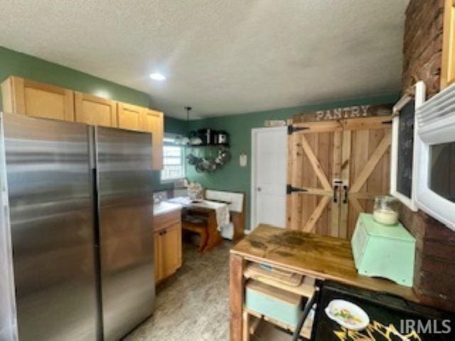 kitchen featuring freestanding refrigerator, a barn door, a textured ceiling, and light brown cabinets