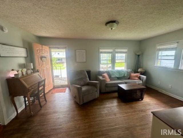 living area with a textured ceiling, wood finished floors, healthy amount of natural light, and baseboards