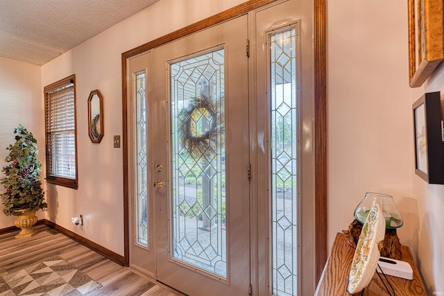 entrance foyer with light wood finished floors, a textured ceiling, and baseboards