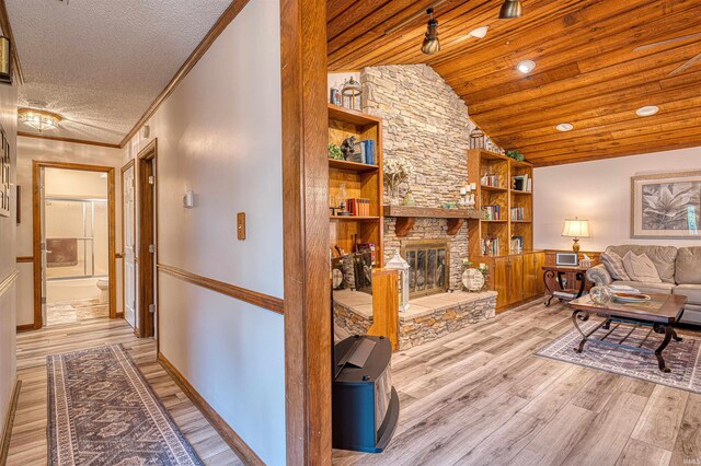 living room with light wood finished floors, built in shelves, a stone fireplace, a textured ceiling, and lofted ceiling