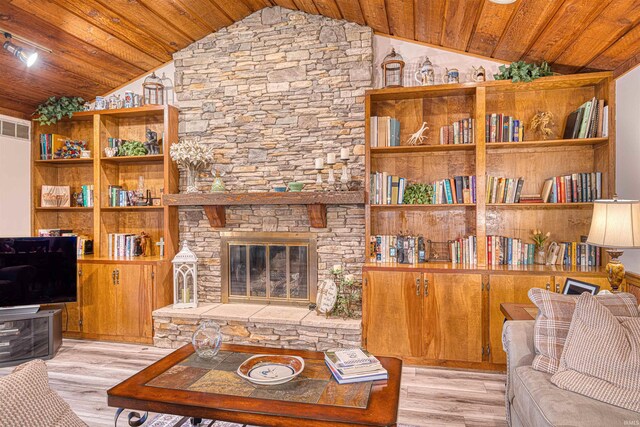 living area featuring vaulted ceiling, wooden ceiling, light wood finished floors, and a stone fireplace