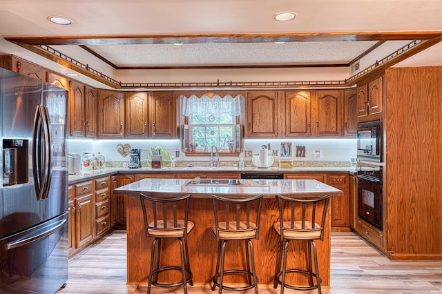 kitchen with black appliances, brown cabinets, a sink, light wood finished floors, and ornamental molding