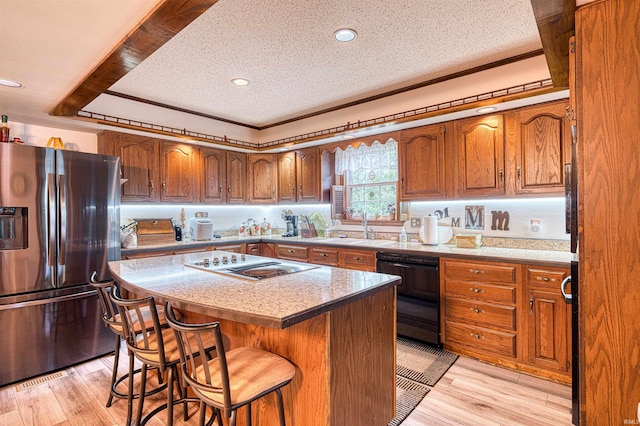 kitchen with black appliances, a sink, a textured ceiling, brown cabinets, and a center island