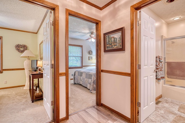 hall with a textured ceiling, ornamental molding, light carpet, baseboards, and light wood-style floors