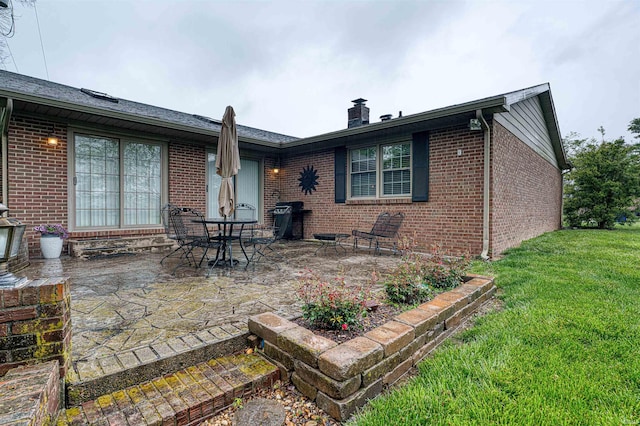back of property featuring a chimney, brick siding, a yard, and a patio area