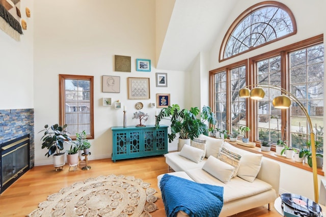 sitting room featuring high vaulted ceiling, wood finished floors, a stone fireplace, and baseboards