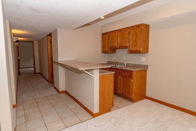kitchen with brown cabinets, a peninsula, a sink, baseboards, and recessed lighting