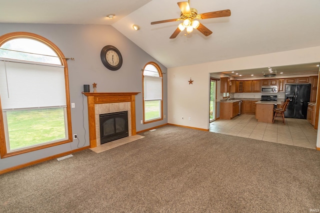 unfurnished living room with a sink, vaulted ceiling, light colored carpet, baseboards, and a tiled fireplace