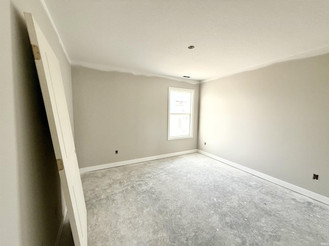 spare room featuring baseboards, ornamental molding, and concrete floors