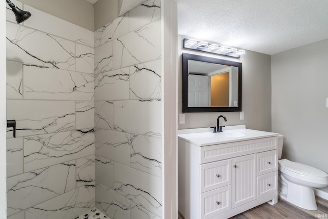 bathroom featuring a marble finish shower, vanity, toilet, a textured ceiling, and wood finished floors