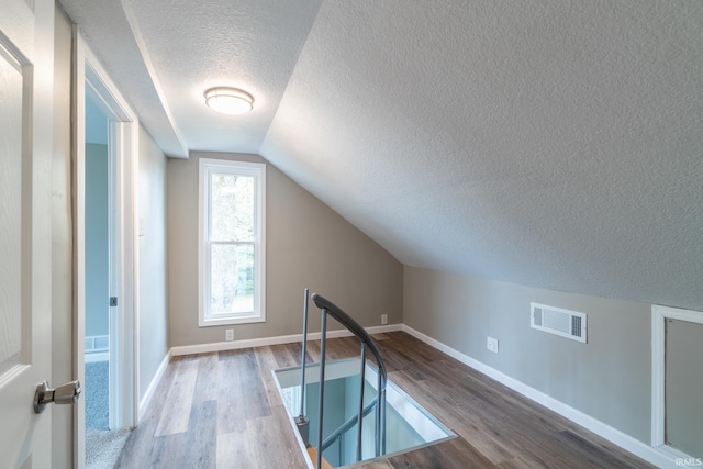 bonus room featuring a textured ceiling, wood finished floors, vaulted ceiling, and baseboards