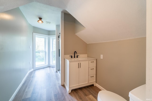 bathroom with toilet, wood finished floors, baseboards, vanity, and vaulted ceiling