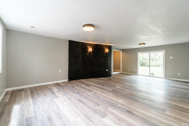 unfurnished living room with wood finished floors, a textured ceiling, and baseboards
