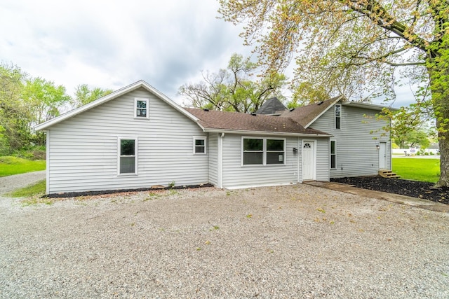 rear view of property featuring gravel driveway and roof with shingles