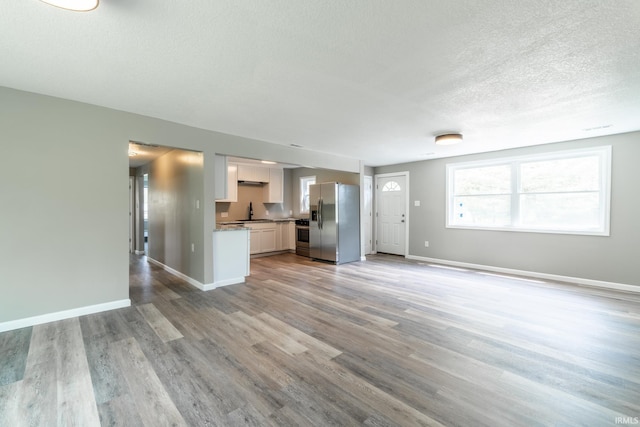 unfurnished living room featuring a textured ceiling, light wood-style flooring, baseboards, and a sink