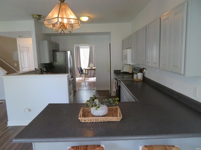 kitchen with electric range oven, white microwave, dark countertops, a chandelier, and a peninsula