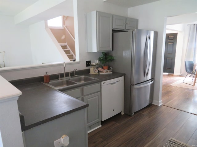 kitchen with white dishwasher, a sink, freestanding refrigerator, dark wood-style flooring, and dark countertops