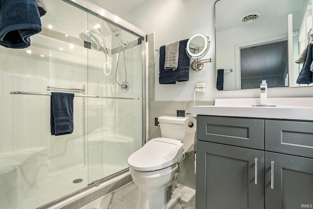bathroom with tile walls, vanity, toilet, a stall shower, and marble look tile flooring