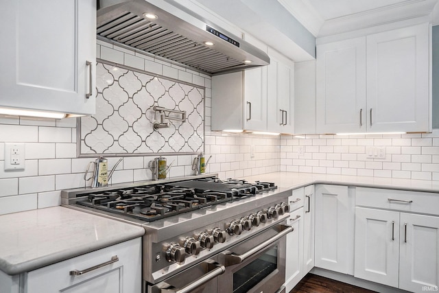 kitchen with range with two ovens, ventilation hood, crown molding, backsplash, and white cabinetry