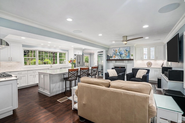 living area with ornamental molding, a brick fireplace, healthy amount of natural light, dark wood-style flooring, and recessed lighting