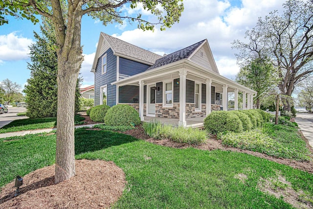 view of home's exterior featuring a shingled roof, a porch, a yard, and stone siding