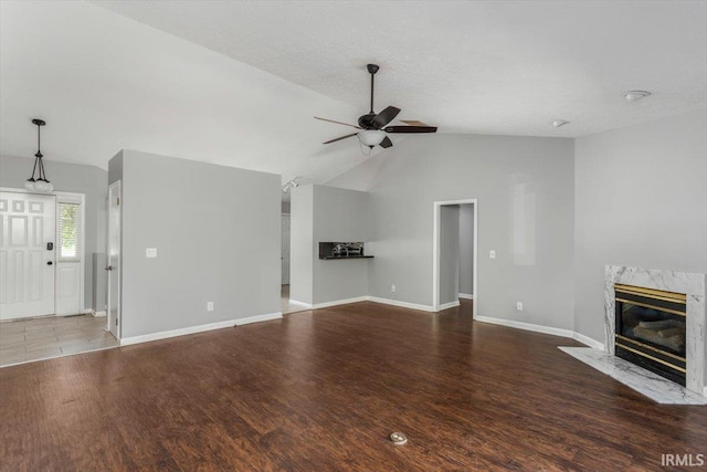 unfurnished living room with ceiling fan, vaulted ceiling, baseboards, wood finished floors, and a fireplace