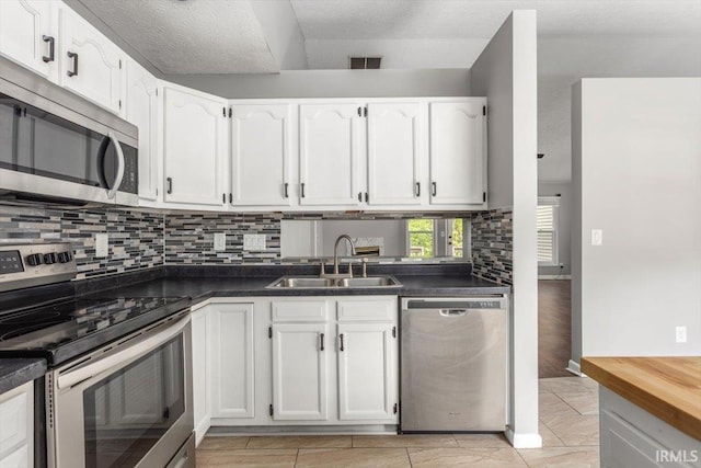 kitchen featuring stainless steel appliances, a sink, white cabinets, backsplash, and dark countertops