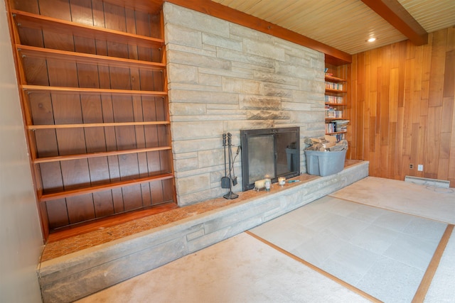 unfurnished living room with a stone fireplace, beam ceiling, wood walls, wood ceiling, and built in features