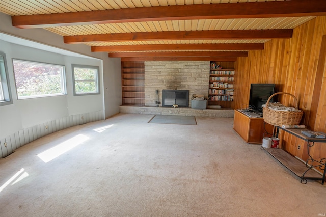 unfurnished living room featuring light colored carpet, beam ceiling, wood ceiling, a stone fireplace, and wooden walls