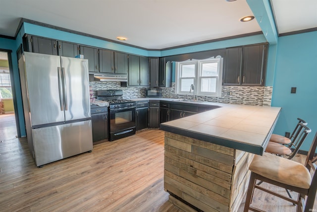 kitchen featuring freestanding refrigerator, black gas range oven, a sink, a peninsula, and under cabinet range hood