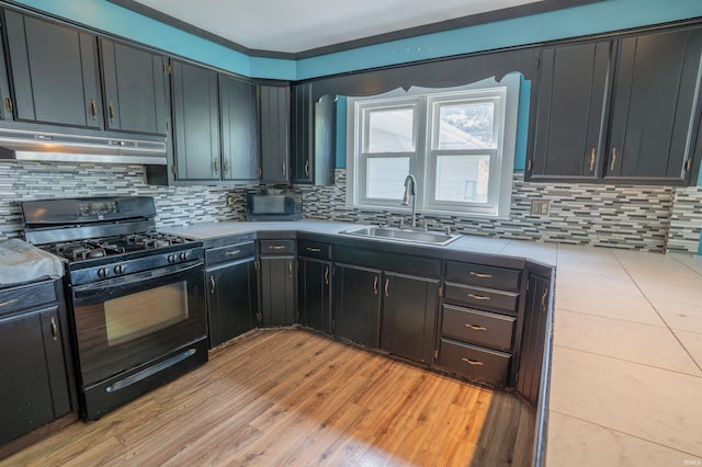 kitchen featuring black gas range oven, under cabinet range hood, a sink, and tasteful backsplash