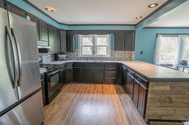 kitchen featuring freestanding refrigerator, a sink, black gas range, a peninsula, and tasteful backsplash
