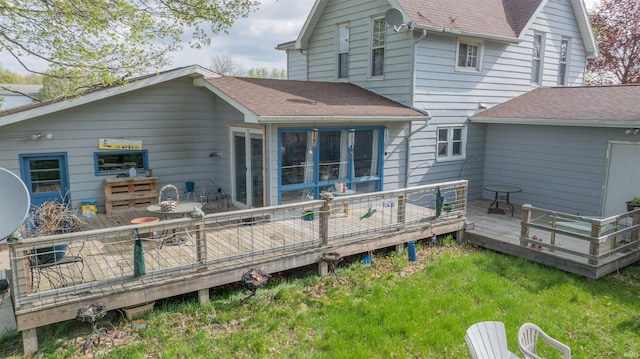 back of property with a shingled roof, a deck, and a yard