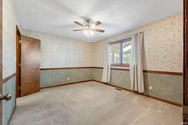 carpeted empty room with wallpapered walls, ceiling fan, and a textured ceiling
