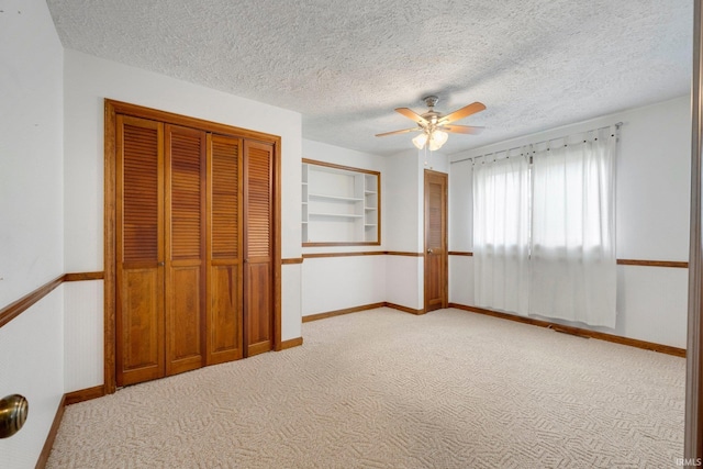 unfurnished bedroom with light carpet, a textured ceiling, a closet, baseboards, and a ceiling fan