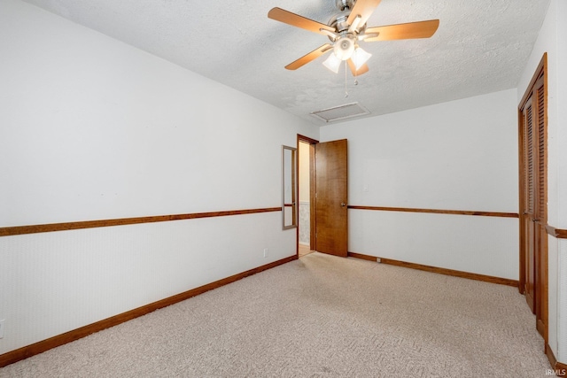 spare room with attic access, light colored carpet, a textured ceiling, ceiling fan, and baseboards