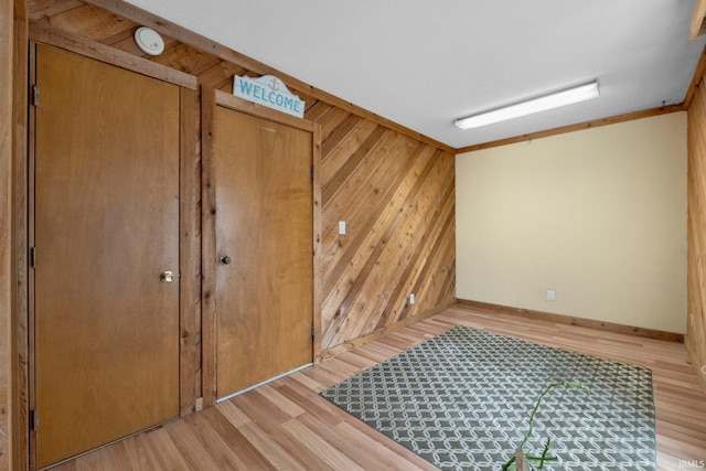 unfurnished room featuring light wood-style floors, wood walls, baseboards, and a smoke detector